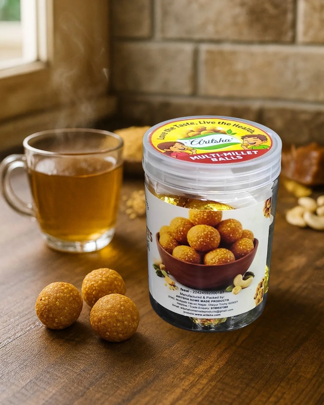 Aritsha Multimillet Urundai jar with millet laddu balls served beside herbal tea on wooden table